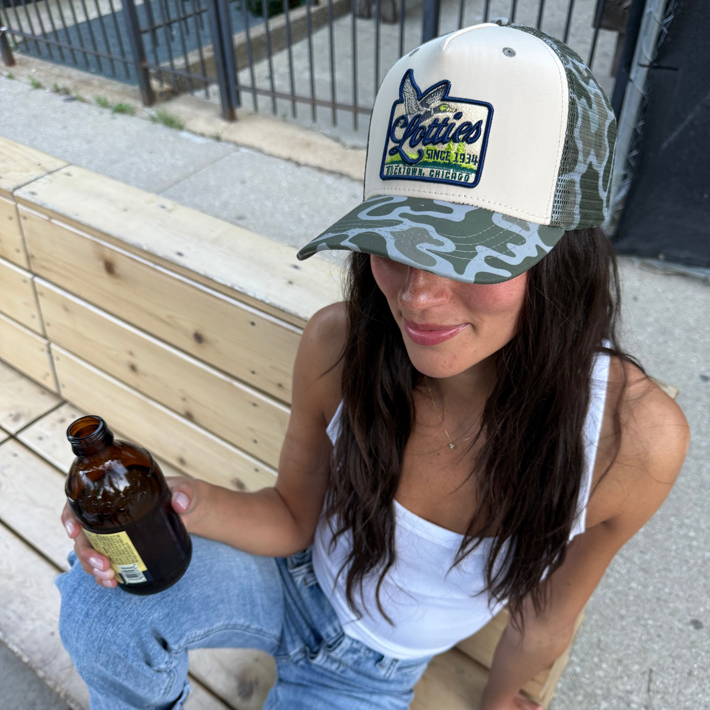 Woman wearing a cap and holding a bottle on a wooden bench.