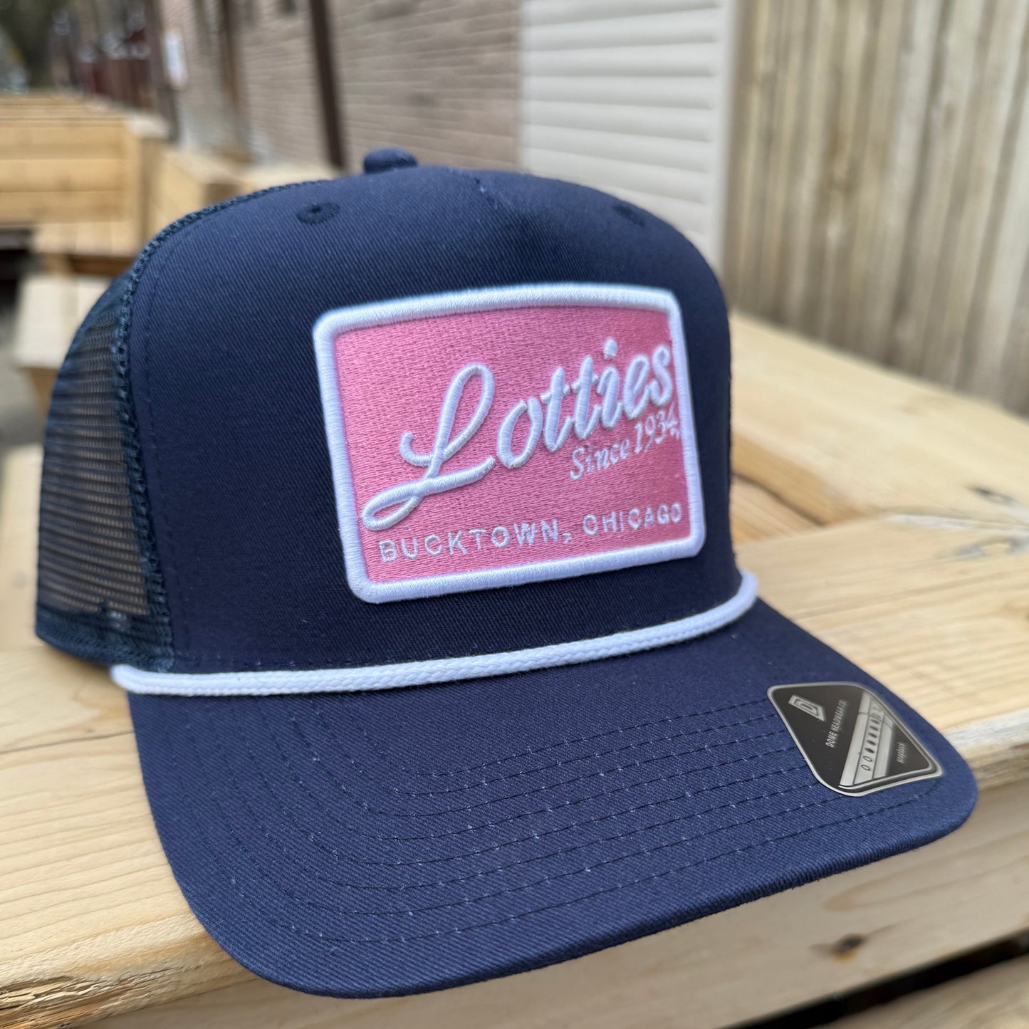 A navy blue cap with a white rope detail around the base and a pink and white 'Lotties' signature patch on the front.