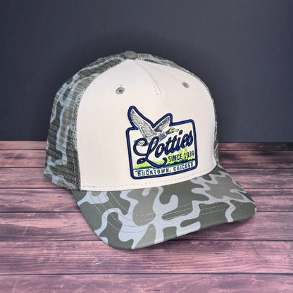Trucker hat with camouflage brim and white front panel on a wooden surface with dark background
