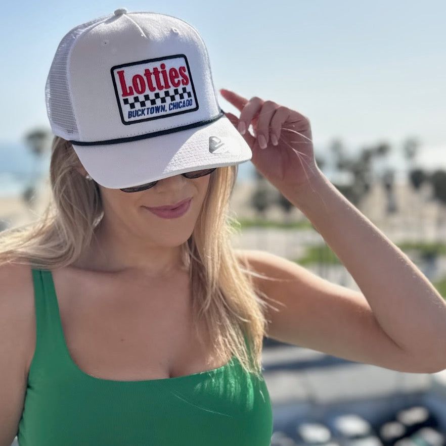 Woman wearing a white cap with 'Lotties Bucktown Chicago' logo and sunglasses, standing outdoors.