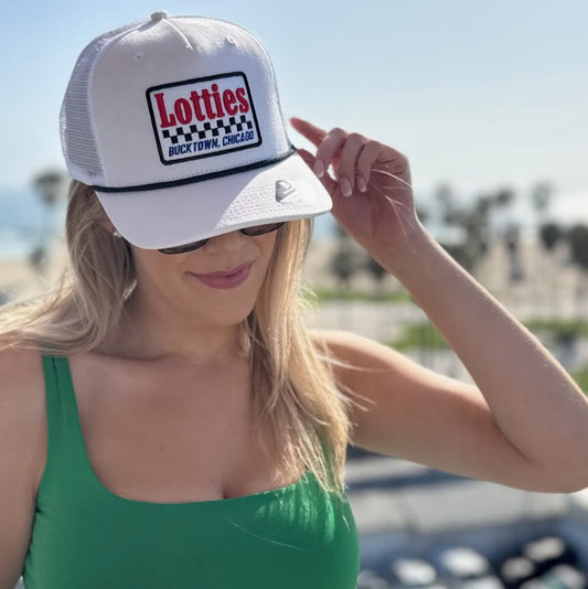 Woman wearing a white cap with 'Lotties Bucktown Chicago' logo and sunglasses, standing outdoors.